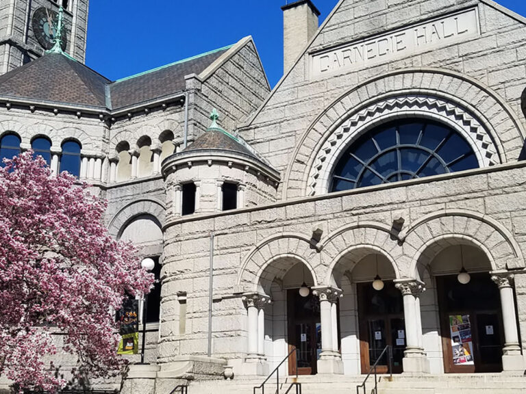 Exterior photo of stone New Hazlett Theater building with pink cherry blossom tree