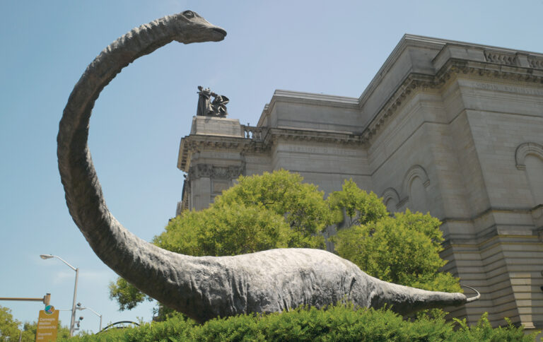 Large statue of long necked dinosaur next to Carnegie Museum of Natural History building